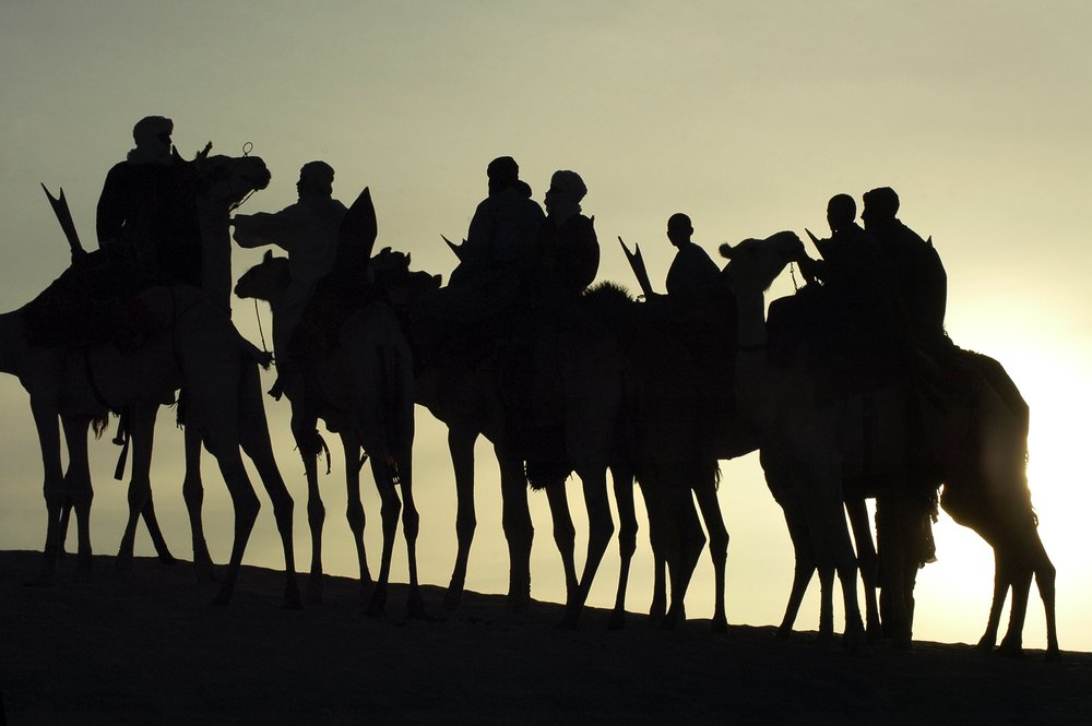 A silhouette of a group of Tuareg on their camels in the desert 